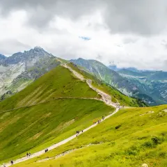 Szlak turystyczny w Tatrach, gdzie w góry w Polsce wędrują tłumy ludzi. Zielone zbocza, skaliste szczyty i chmury na niebie.