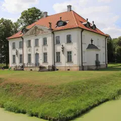 Pałac w Choroszczy otoczony fosą i zielenią, z drewnianym mostkiem prowadzącym do rezydencji.