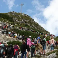 Tłum turystów wspina się po kamienistym szlaku na Giewont. W oddali widać krzyż.
