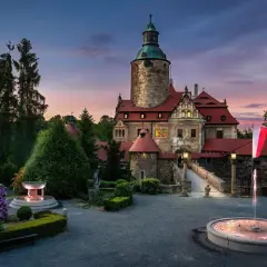 Zamek Czocha o zmierzchu, z fontannami i kwitnącymi rododendronami. Bilety do zamku można kupić online.