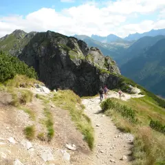 Turyści idą kamienistym szlakiem w Tatrach. Widok na góry i lasy. Idealne tatry szlaki dla średnio zaawansowanych.