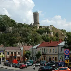 Ruiny iłża zamek górują nad miasteczkiem. W dole widać ulicę z samochodami i kolorowe kamienice.