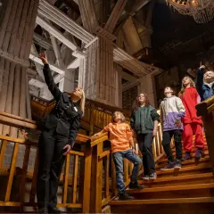 Przewodniczka oprowadza grupę dzieci po Kopalni Soli "Wieliczka". Wszyscy są ubrani na cebulkę, co sugeruje stałą, niską temperaturę w kopalni.