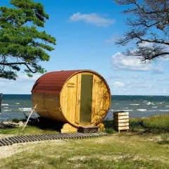 Drewniana beczka-sauna na plaży, jak królowa Bałtyku, wita gości. W tle morze i niebo.
