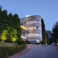 Rezydencja Izabella nocą. Elegancka budowla z podświetlanymi żywopłotami i parkingiem.