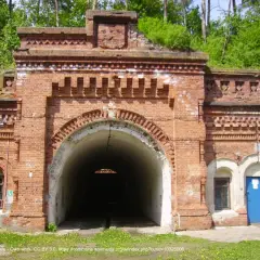 Wejście do tunelu w ceglanej twierdzy Osowiec. Zarośnięte zielenią mury i łukowate przejście.