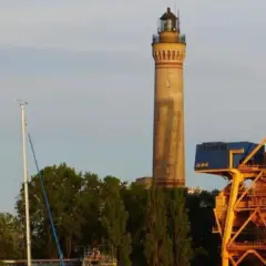 Najwyższa latarnia morska w Polsce, strzegąca portu, góruje nad żółtymi dźwigami i zielenią.
