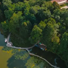 Widok z lotu ptaka na jezioro z żaglówką, drewnianą kładką i otaczającym lasem.
