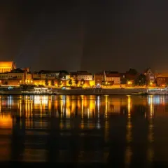 Nocny widok na oświetlony bulwar w Toruniu z odbiciem świateł w Wiśle.