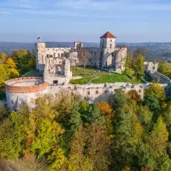 Ruiny zamków Orlich Gniazd na wzgórzu, otoczone jesiennym lasem. Polska flaga powiewa na wieży.