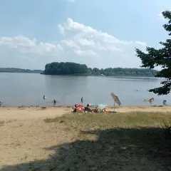 Słoneczny dzień nad jeziorem przeczyckim. Ludzie odpoczywają na plaży i kąpią się w wodzie.
