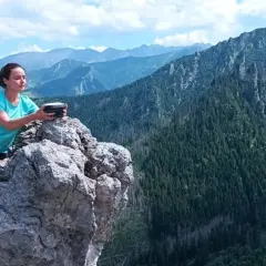 Kobieta na skale z urządzeniem w rękach, podziwia rozległą panoramę górską. Widok zapiera dech w piersiach, to prawdziwa przełęcz w tatrach wysokich.