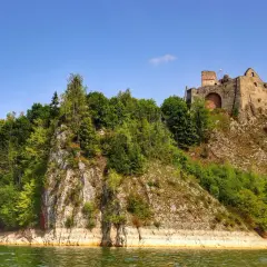 Ruiny zamku na wzgórzu nad zieloną wodą. W tle błękitne niebo. Zalew czorsztyński zachwyca.