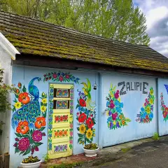 Kolorowy dom w Zalipiu ozdobiony malowidłami kwiatów i pawia. Na ścianie widnieje napis "Zalipie cennik".