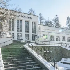 Zimowy dzień w Szczawnicy. Biały budynek sanatorium z napisem "Sanatorium" i schody pokryte śniegiem. Idealne miejsce na relaks w termach.