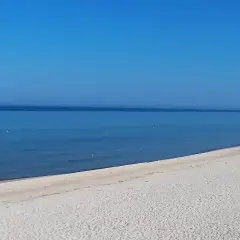 Grzybowo nadmorskie: zejście na plażę. Dwie osoby spacerują po piaszczystej plaży, morze i błękitne niebo.