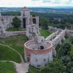 Ruiny zamku Tenczynek na wzgórzu, otoczone zielenią. Widoczna okrągła baszta i fragmenty murów obronnych.