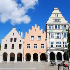 Kolorowe kamienice na olsztyńskim rynku, z arkadami i ozdobnymi fasadami, pod błękitnym niebem.