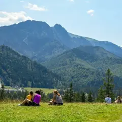 Ludzie odpoczywają na trawie, podziwiając panoramę Tatr z widoczną skocznią narciarską Wielka Krokiew.