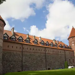 Zamek w Bytowie, z kamiennymi murami i ceglanymi wieżami, prezentuje się majestatycznie pod błękitnym niebem z chmurami.