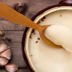 Gęsi smalec w glinianym naczyniu, drewniana łyżka ze smalcem, czosnek na drewnianym tle.