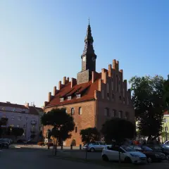 Ratusz w mieście nad jeziorem Skiertąg, z charakterystyczną wieżą zegarową, otoczony kolorowymi kamienicami i zielenią.