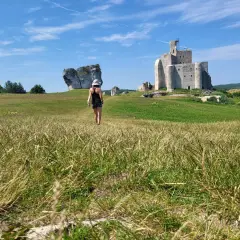 Kobieta idzie przez łąkę w kierunku ruin zamku na Szlaku Orlich Gniazd.
