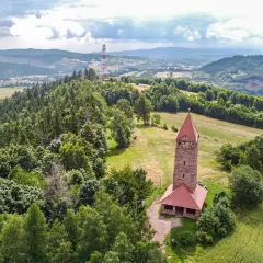 Kamienna wieża widokowa na wzgórzu, otoczona lasami i polami. Jedna z wielu wież widokowych na Dolnym Śląsku, oferująca piękne krajobrazy.