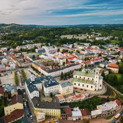 Urokliwe miasto w dolinie ropy, z dominującą białą bazyliką i kolorowymi kamienicami, otoczone zielonymi wzgórzami.