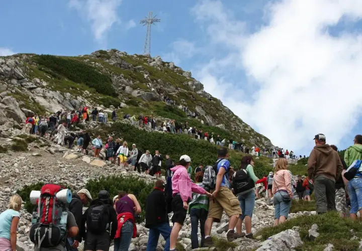 Tłum turystów wspina się po kamienistym szlaku na Giewont. W oddali widać krzyż.