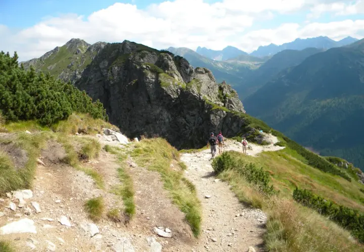 Turyści idą kamienistym szlakiem w Tatrach. Widok na góry i lasy. Idealne tatry szlaki dla średnio zaawansowanych.