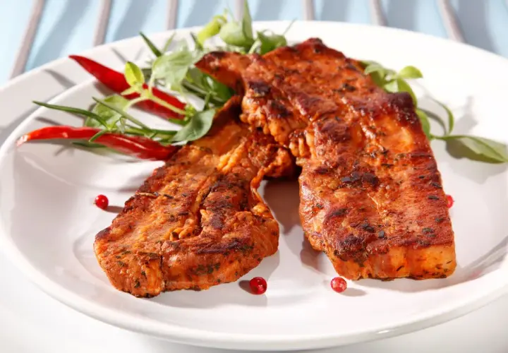 Dwa soczyste plastry boczek na grilla, przyprawione ziołami i podane z papryczkami chili.