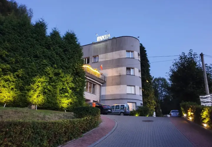 Rezydencja Izabella nocą. Elegancka budowla z podświetlanymi żywopłotami i parkingiem.