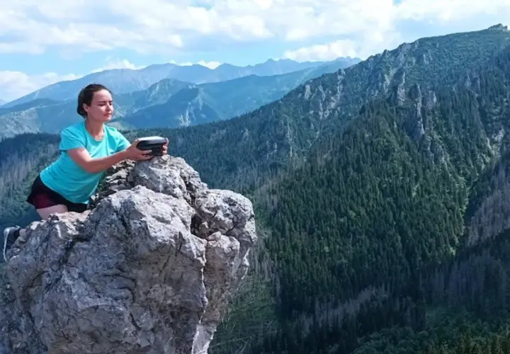 Kobieta na skale z urządzeniem w rękach, podziwia rozległą panoramę górską. Widok zapiera dech w piersiach, to prawdziwa przełęcz w tatrach wysokich.