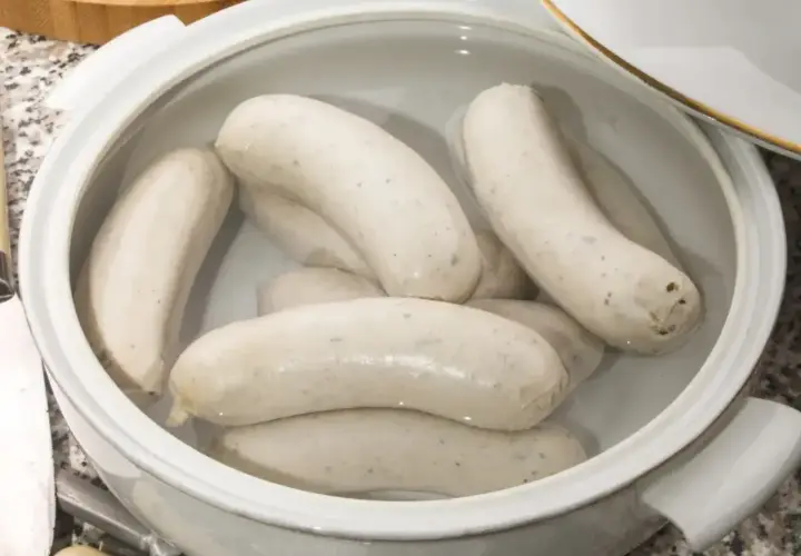 Kilka białych kiełbasek parzonych w garnku, gotowych do podania.