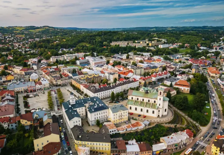 Urokliwe miasto w dolinie ropy, z dominującą białą bazyliką i kolorowymi kamienicami, otoczone zielonymi wzgórzami.