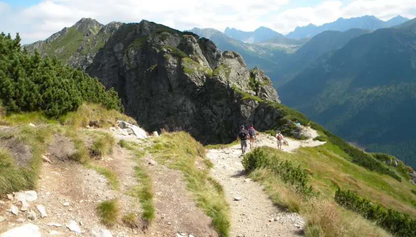Turyści idą kamienistym szlakiem w Tatrach. Widok na góry i lasy. Idealne tatry szlaki dla średnio zaawansowanych.