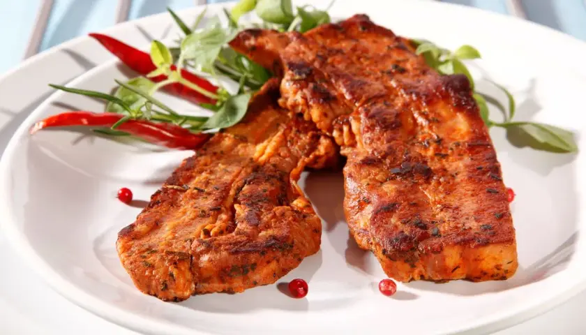 Dwa soczyste plastry boczek na grilla, przyprawione ziołami i podane z papryczkami chili.