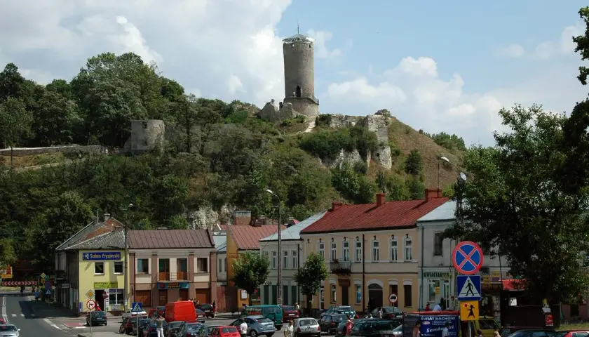 Ruiny iłża zamek górują nad miasteczkiem. W dole widać ulicę z samochodami i kolorowe kamienice.