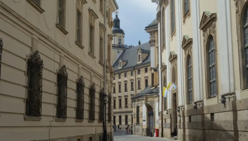Wąska, brukowana uliczka prowadzi do serca starego rynku we Wrocławiu. Po bokach piętrzą się zabytkowe kamienice z ozdobnymi fasadami i kratami w oknach.
