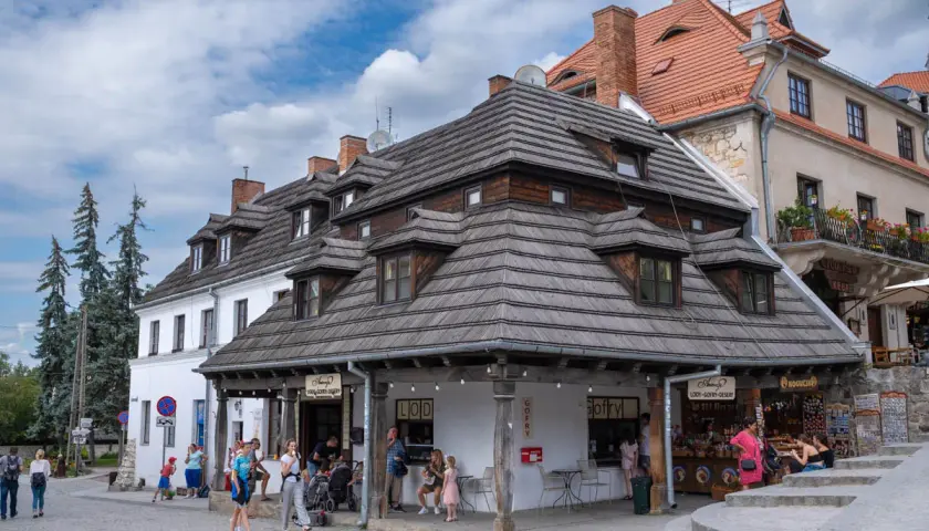 Tętniący życiem rynek w Kazimierzu Dolnym. Ludzie spacerują, kupują lody i gofry, podziwiając zabytkową architekturę.