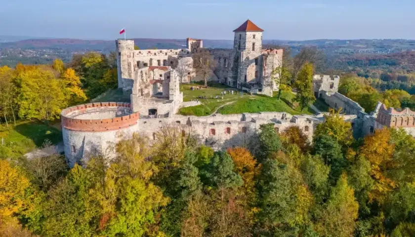 Ruiny zamków Orlich Gniazd na wzgórzu, otoczone jesiennym lasem. Polska flaga powiewa na wieży.