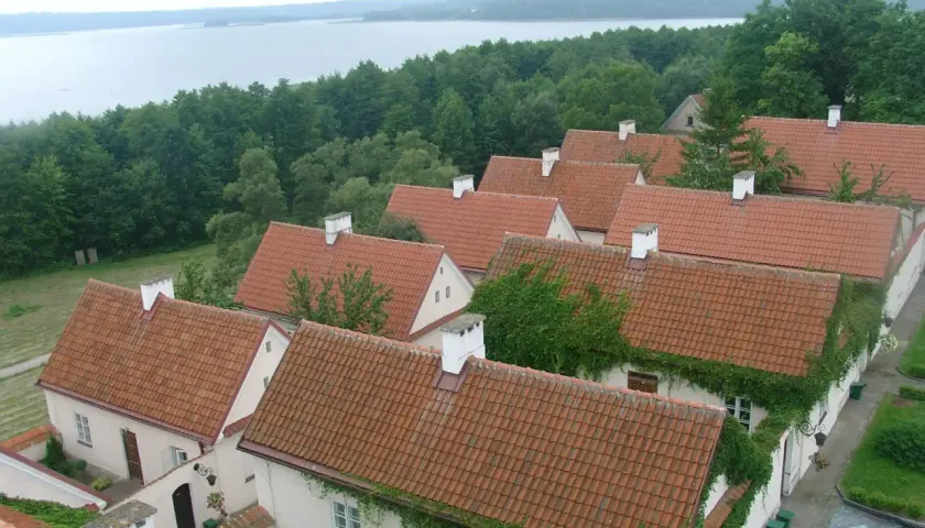 Urokliwe, pokryte czerwonymi dachówkami domy w Sejnach, otoczone zielenią, z widokiem na jezioro. Atrakcje regionu.