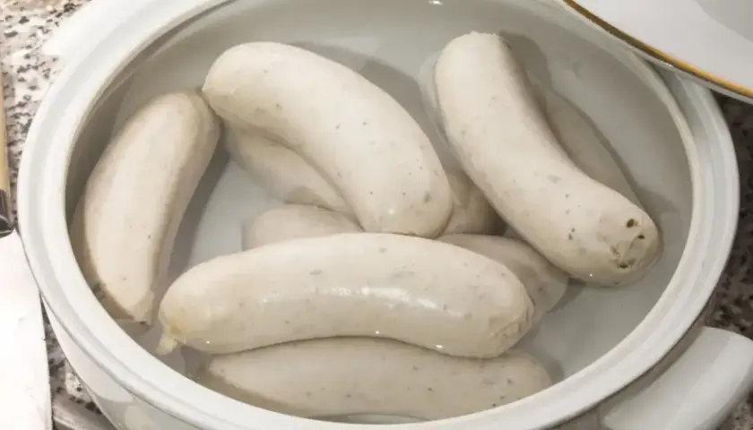 Kilka białych kiełbasek parzonych w garnku, gotowych do podania.