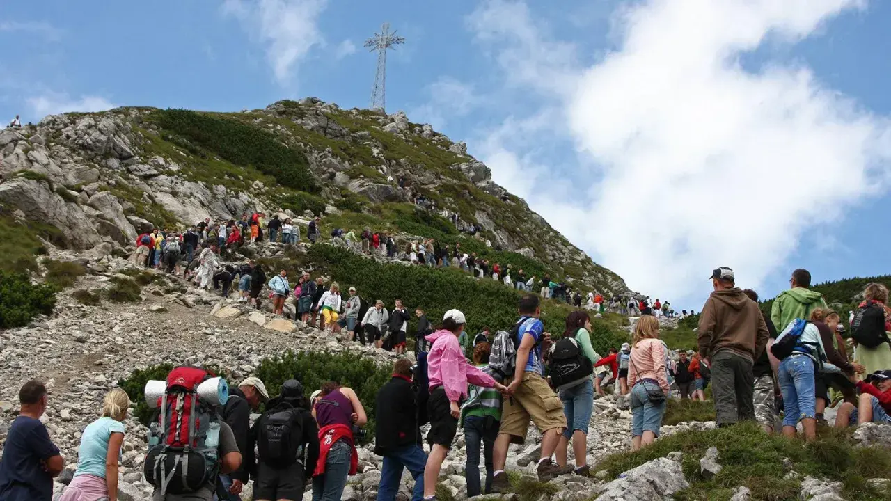 Tłum turystów wspina się po kamienistym szlaku na Giewont. W oddali widać krzyż.