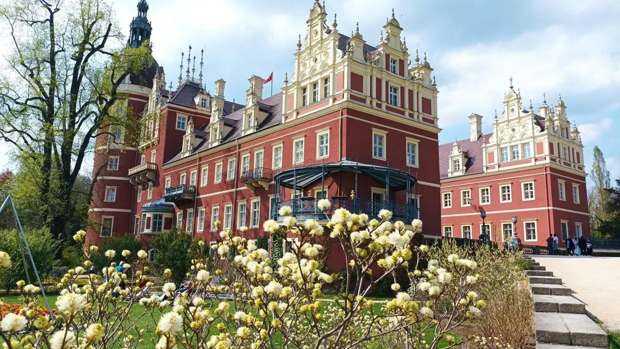 Piękny park mużakowski zwiedzanie w otoczeniu czerwonego pałacu i kwitnących krzewów.
