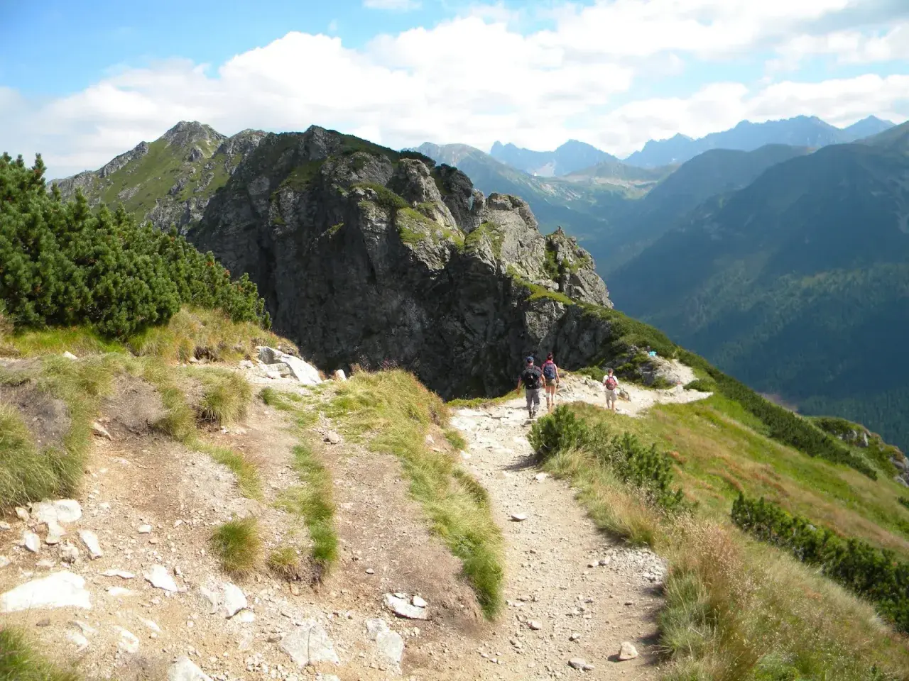 Turyści idą kamienistym szlakiem w Tatrach. Widok na góry i lasy. Idealne tatry szlaki dla średnio zaawansowanych.