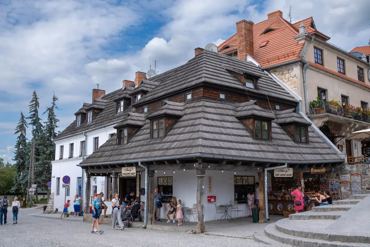Tętniący życiem rynek w Kazimierzu Dolnym. Ludzie spacerują, kupują lody i gofry, podziwiając zabytkową architekturę.