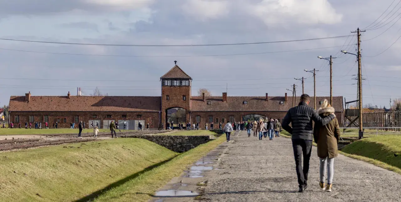 Ludzie spacerują po terenie byłego obozu Auschwitz. To miejsce pamięci, gdzie kiedyś znajdował się obóz zagłady.