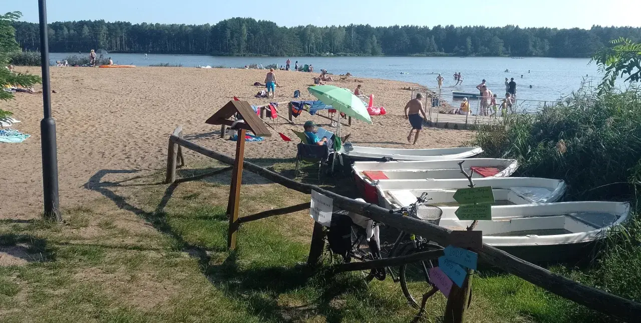 Słoneczny dzień nad zalewem zielona. Ludzie odpoczywają na plaży, kąpią się, a obok stoją łódki.